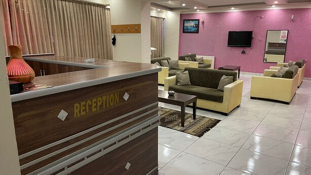 A reception area with a wooden desk labeled "RECEPTION," a living room with sofas and a TV, and a pink wall with a painting. - AŞKALE BİZİM OTEL (Askale)
