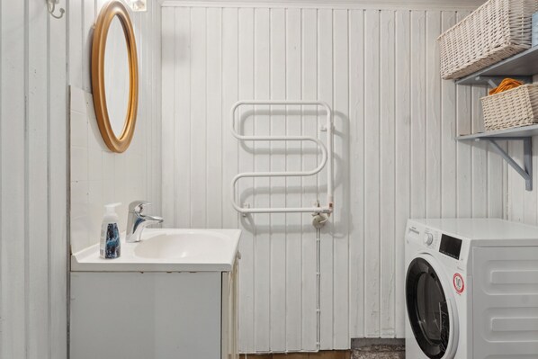 A bathroom with a sink, mirror, towel rack, and a washing machine.