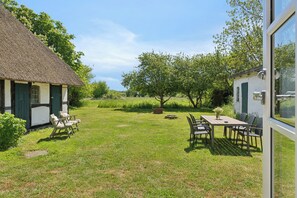 Una casa con tetto di paglia, un giardino, un tavolo con sedie e un piccolo capanno.