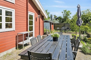 Une terrasse en bois avec une table et des chaises, un banc et un pot de fleurs.