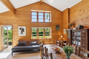 L’intérieur d’un chalet en bois, avec un lit en mezzanine, une table à manger avec des chaises, une bibliothèque et de grandes fenêtres.