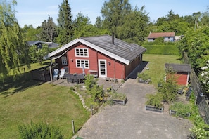 Ein rotes Haus mit Satteldach, einer Veranda und einem kleinen Garten mit Pflanzen und einer Bank.