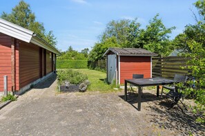 Ein rotes Holzgebäude mit Schuppen, befestigtem Platz und einem Tisch mit Stühlen.
