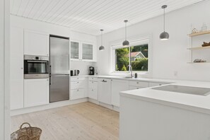 A modern kitchen with white cabinetry, stainless steel appliances, a large window, and pendant lighting.