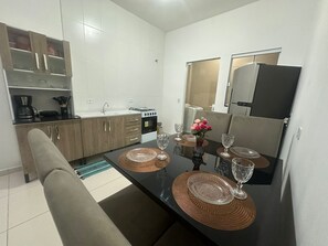 A compact kitchen with a dining table set for four, equipped with a coffee maker, stove, and refrigerator.