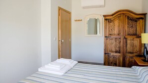 Ett hotellrum med en säng, en garderob i trä, en spegel och en väggmonterad luftkonditioneringsanläggning.