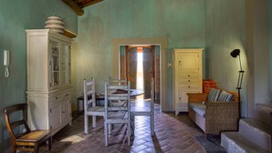 A dining area with a herringbone floor, wooden chairs, a white cabinet with glass doors, a wicker sofa, and a lamp. - MURTA PEQUENA T2 with private pool (Marvão)