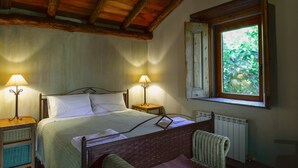 A bedroom with a wooden ceiling, a bed with a metal frame, two bedside lamps, a window with an open shutter, and a radiator below the window. - MURTA PEQUENA T2 with private pool (Marvão)