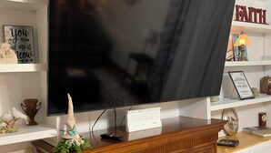 A living room with a flat-screen TV mounted on a wooden cabinet, a fireplace, and shelves with various decorations. - Charming 4-bedroom home with WiFi, AC ,  deck and firepit in delightful Montross (Montross)