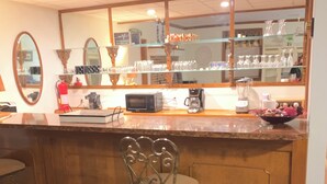 A bar area with a wooden counter, a microwave, a coffee maker, and a bowl of fruit. There is a chair and a patterned rug on the floor. - Charming 4-bedroom home with WiFi, AC ,  deck and firepit in delightful Montross (Montross)