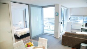Een moderne hotelkamer met een bed, een zithoek met een glazen tafel, een bank en uitzicht op het omliggende landschap.