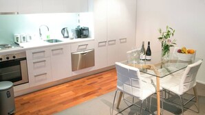Een moderne keuken met witte kasten, een RVS vaatwasser en een glazen eettafel met witte stoelen.