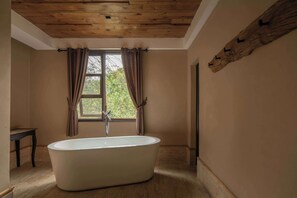 Une salle de bain avec une baignoire sur pieds, un plafond en bois et une fenêtre avec des rideaux.