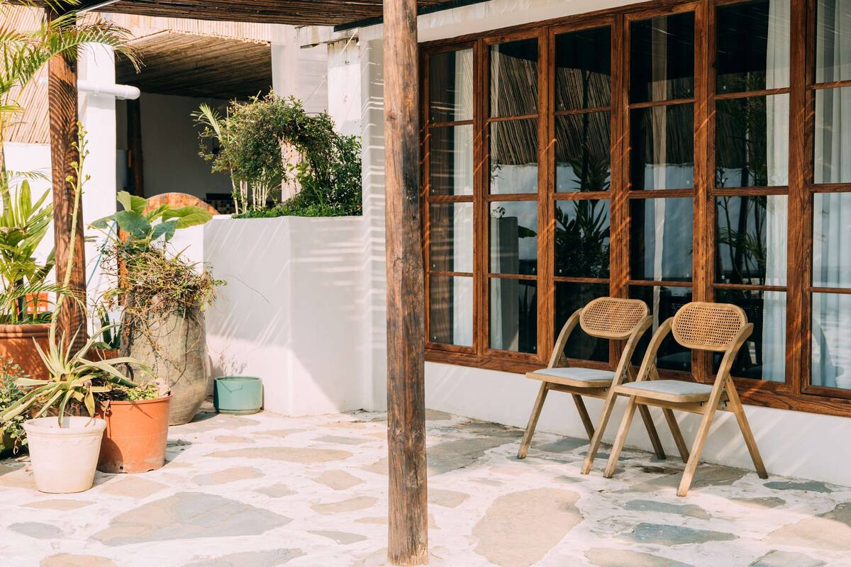 A patio area with stone flooring, wooden chairs, and potted plants.