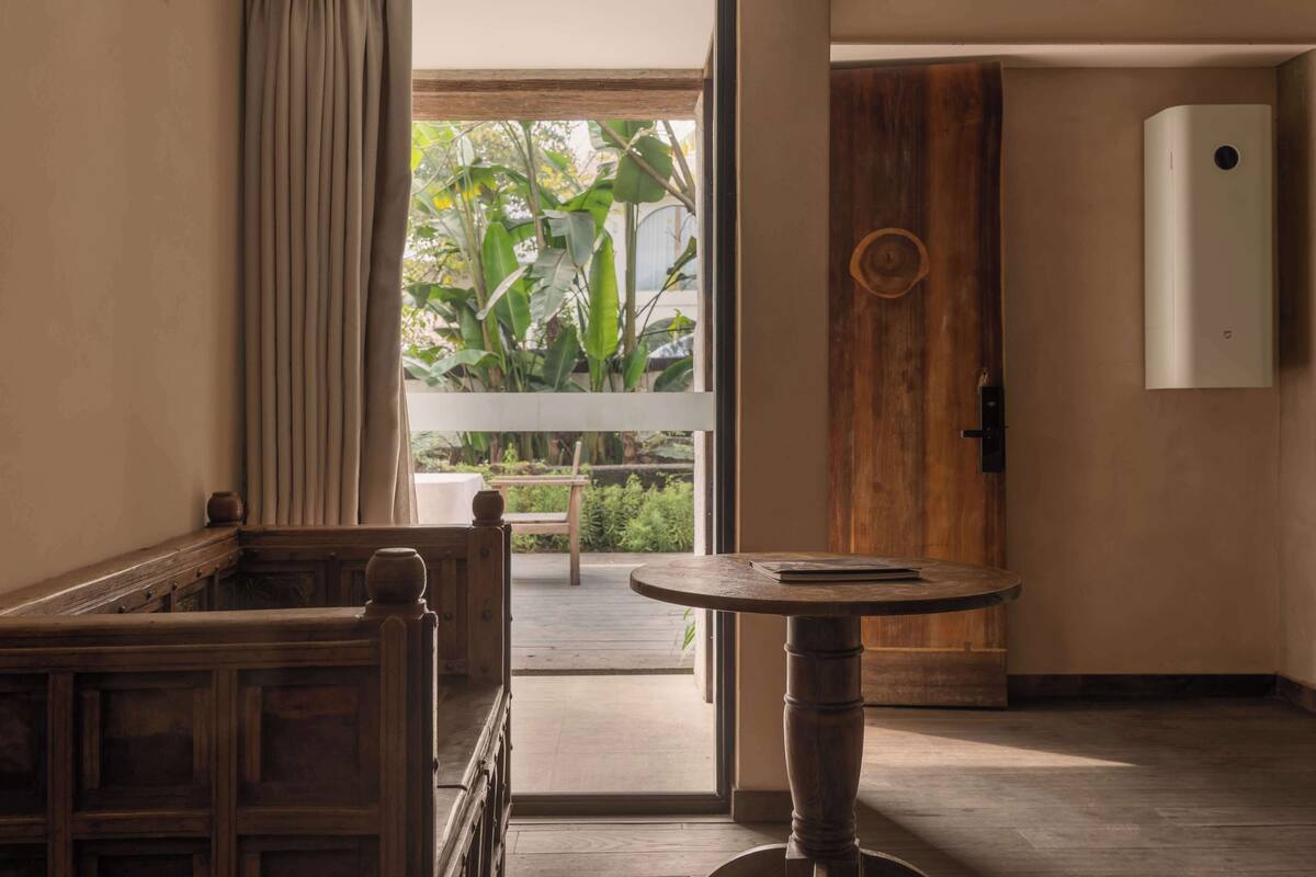 A room with a wooden bench, a round table, and a door leading to a balcony with plants.