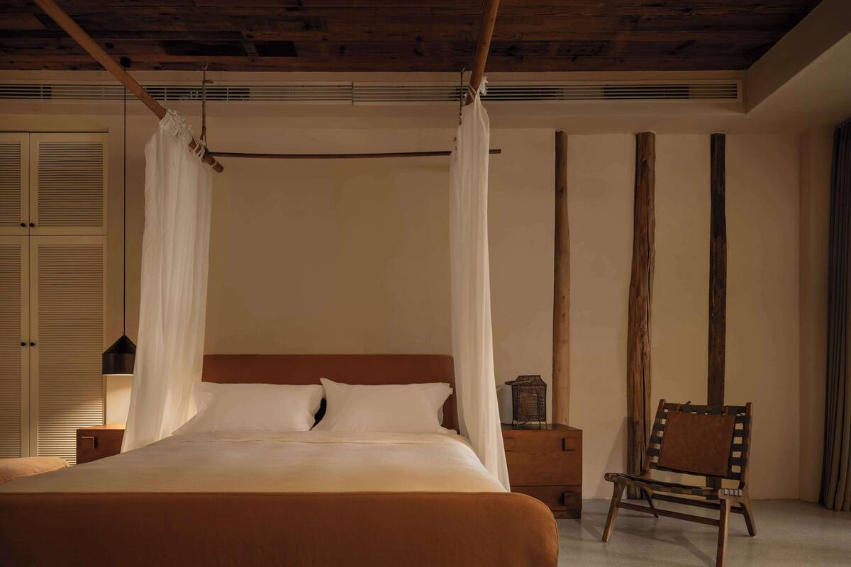 A bedroom with a four-poster bed, a wooden chair, and a nightstand.