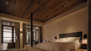 A bedroom with a wooden ceiling, a large bed, a desk, and a window with curtains. - YueLore Retreat (Chengdu)