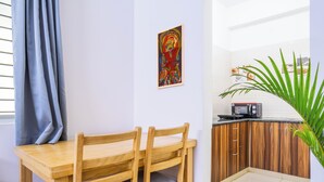 Un comedor con una mesa y sillas de madera, un cuadro en la pared, y una cocina con armarios de madera y un microondas.