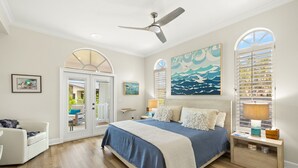 A bedroom with a bed, a ceiling fan, a nightstand, a lamp, and a painting. - Gorgeous New pool home a bike ride from beach! (Sanibel)