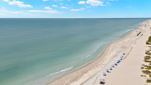 A beach with rows of umbrellas and beach chairs along the shoreline. - Gorgeous New pool home a bike ride from beach! (Sanibel)