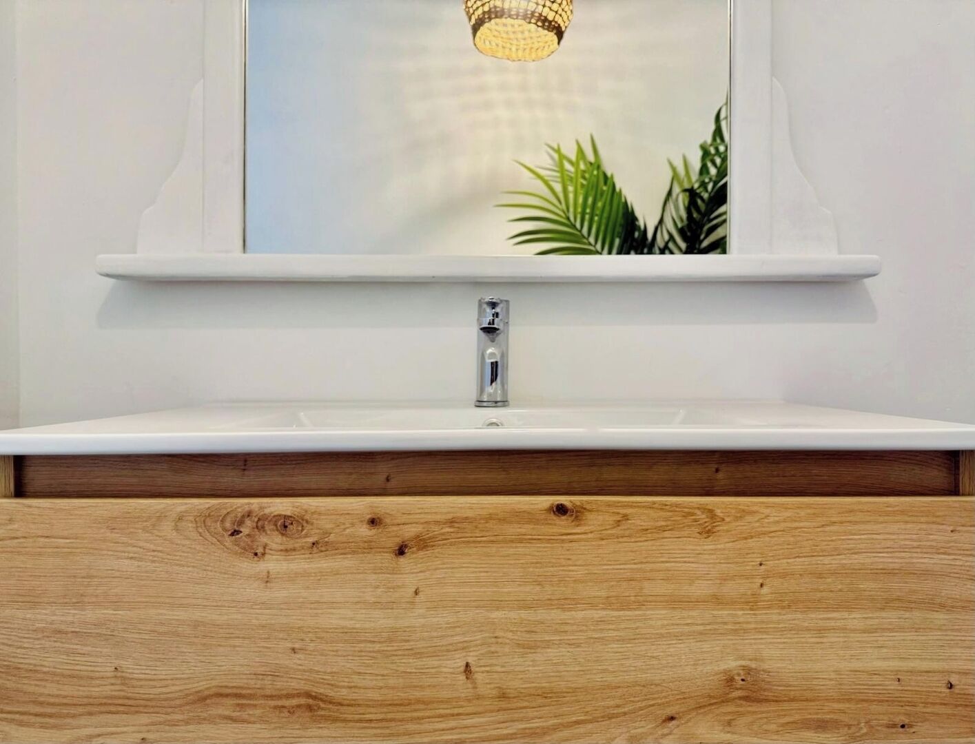 Une salle de bain avec un lavabo blanc, un meuble-lavabo en bois et un miroir au-dessus du lavabo.