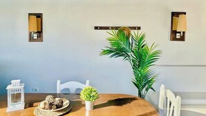 A dining area with a wooden table, chairs, a potted plant, and wall-mounted lamps.