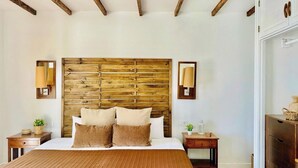 A bedroom with a wooden headboard, two bedside lamps, a bed with brown bedding, and a wooden nightstand with a plant.