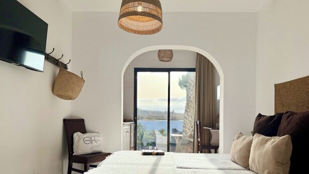 Un dormitorio con una cama grande, un televisor montado en la pared, una lámpara de mimbre y vistas a través de un arco.