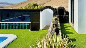 Una casa moderna con piscina, un arco de piedra y vistas a una colina.