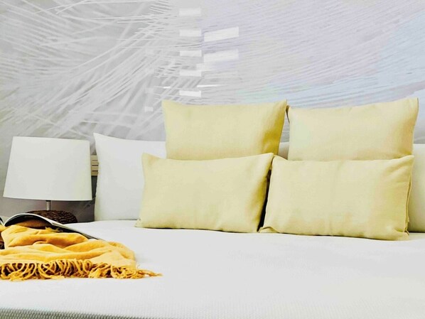 Ein ordentlich bezogenes Bett mit vier Kissen, einer Nachttischlampe und einer gelben Tagesdecke.