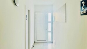 Un pasillo con una puerta al final, un letrero con el número '2' y una lámpara fijada a la pared.