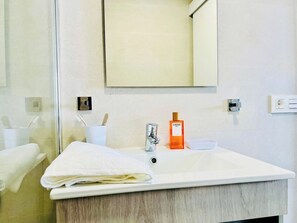 Ein Badezimmer mit weißem Waschbecken, einem Spiegel darüber, einer Seife und einem Handtuch auf der Ablagefläche.