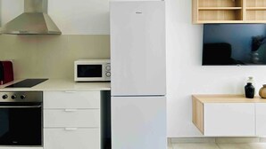Una cocina moderna con un refrigerador blanco, un microondas y una estufa. Hay un mueble de madera con un televisor encima.