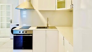 A compact kitchen with a built-in oven, a stove, a sink, and white cabinetry.