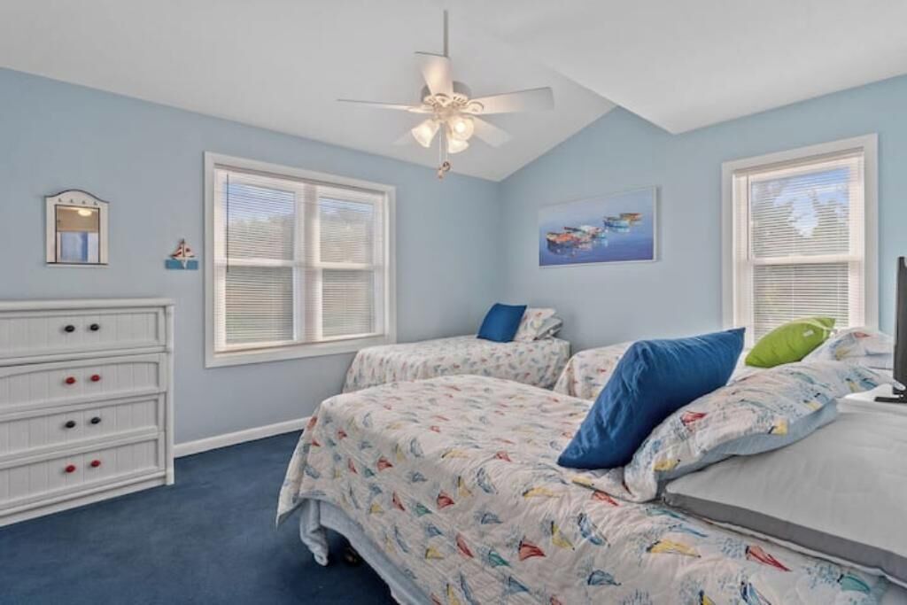 Une chambre avec deux lits, un ventilateur de plafond, une commode et une fenêtre avec des stores.