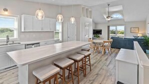 A modern kitchen with a large island, wooden bar stools, pendant lighting, and a view of the outdoors. - Everyone can relax at Salt Life (Topsail Beach)