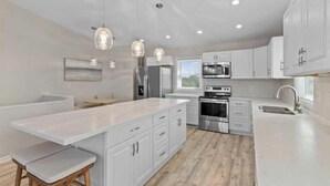 A modern kitchen with white cabinetry, a central island, pendant lighting, and a view of the outdoors. - Everyone can relax at Salt Life (Topsail Beach)
