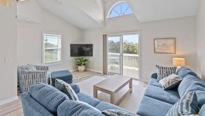 A spacious living room with a ceiling fan, a flat-screen TV, a large window, and a balcony. - Everyone can relax at Salt Life (Topsail Beach)