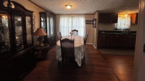 A dining area with a table set for two, a cabinet with glass doors, and a kitchen area with a window.