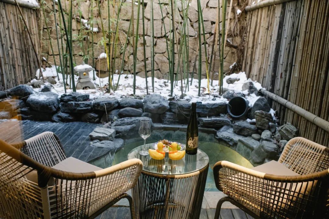 A glass-top table with chairs in a garden setting with a stone wall and bamboo plants.