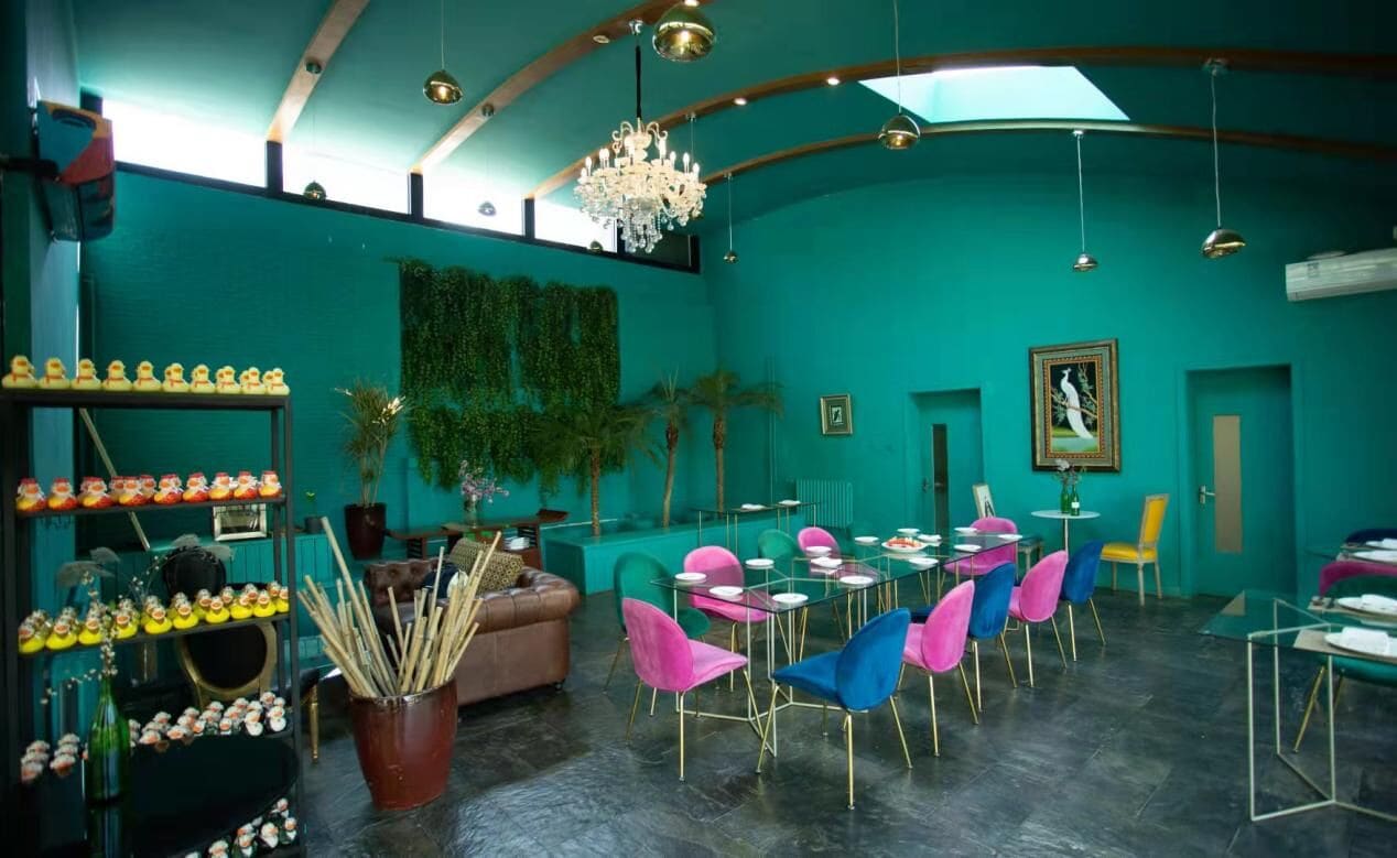 Un restaurant à la décoration turquoise, agrémenté d’un lustre, de chaises colorées et d’un espace repas.