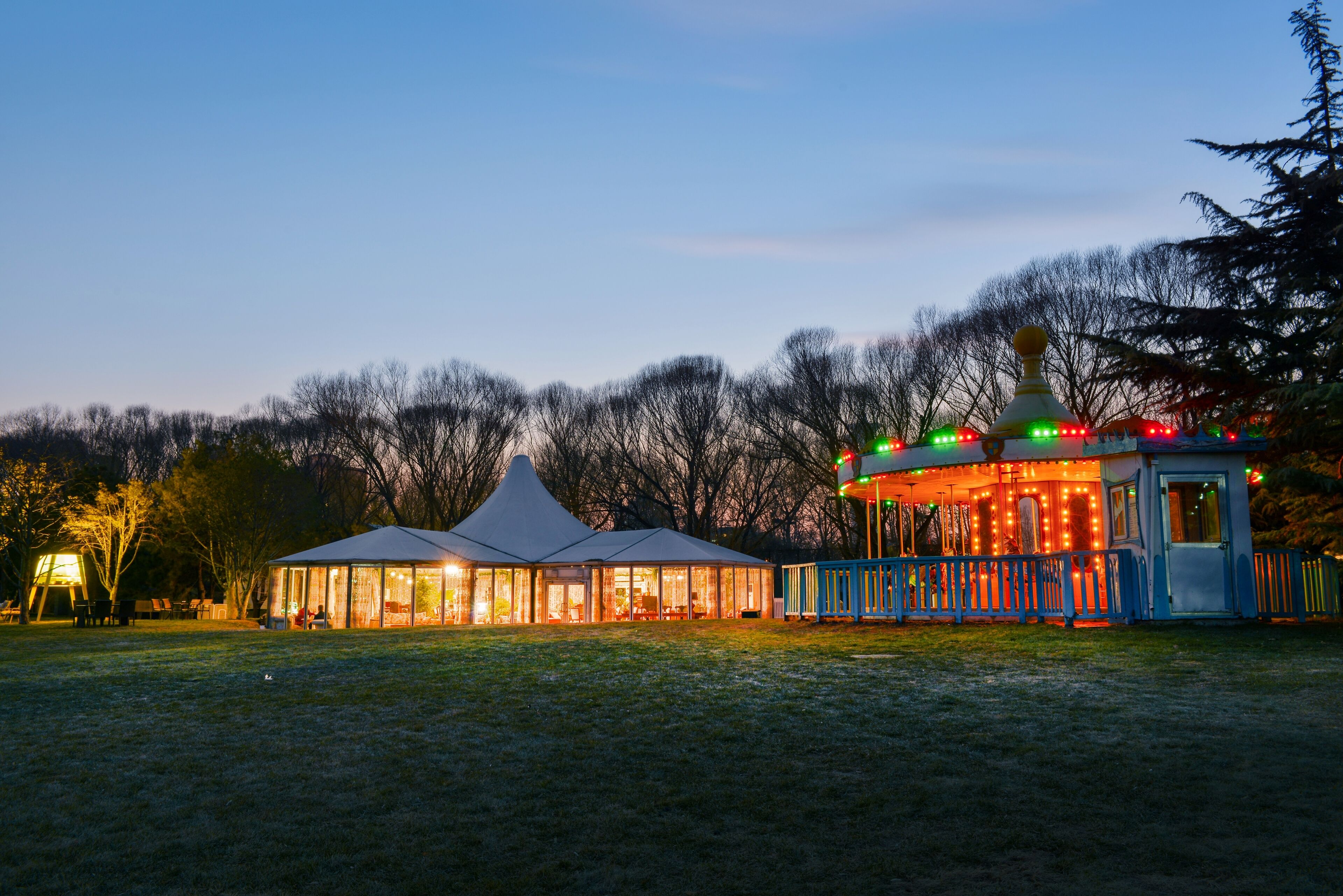 A building with a glass facade and a white roof, surrounded by a blue fence with colorful lights.