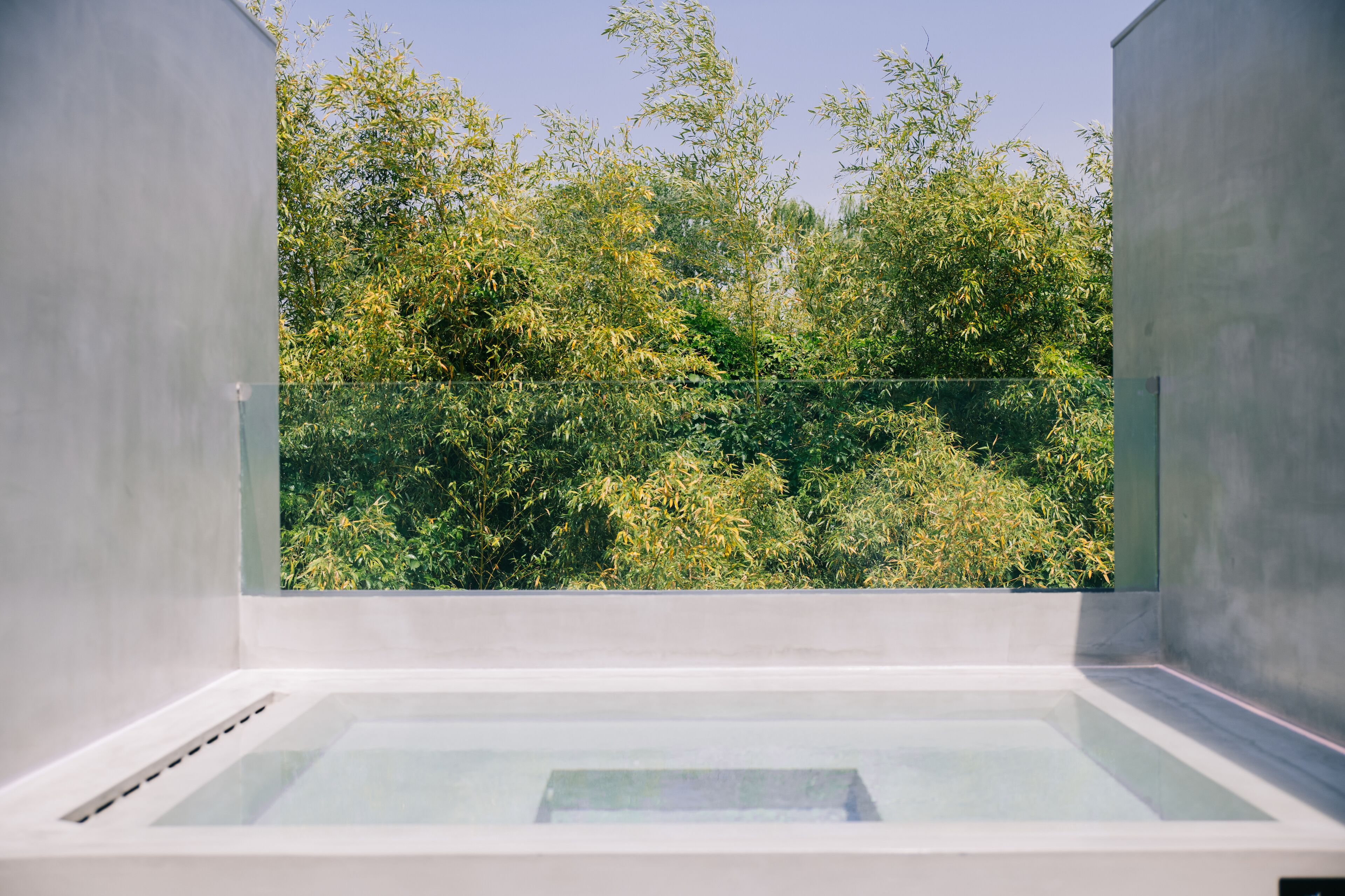 Un spa moderne doté d'un jacuzzi à ciel ouvert, protégé par des parois de verre, et offrant une vue sur une végétation luxuriante.