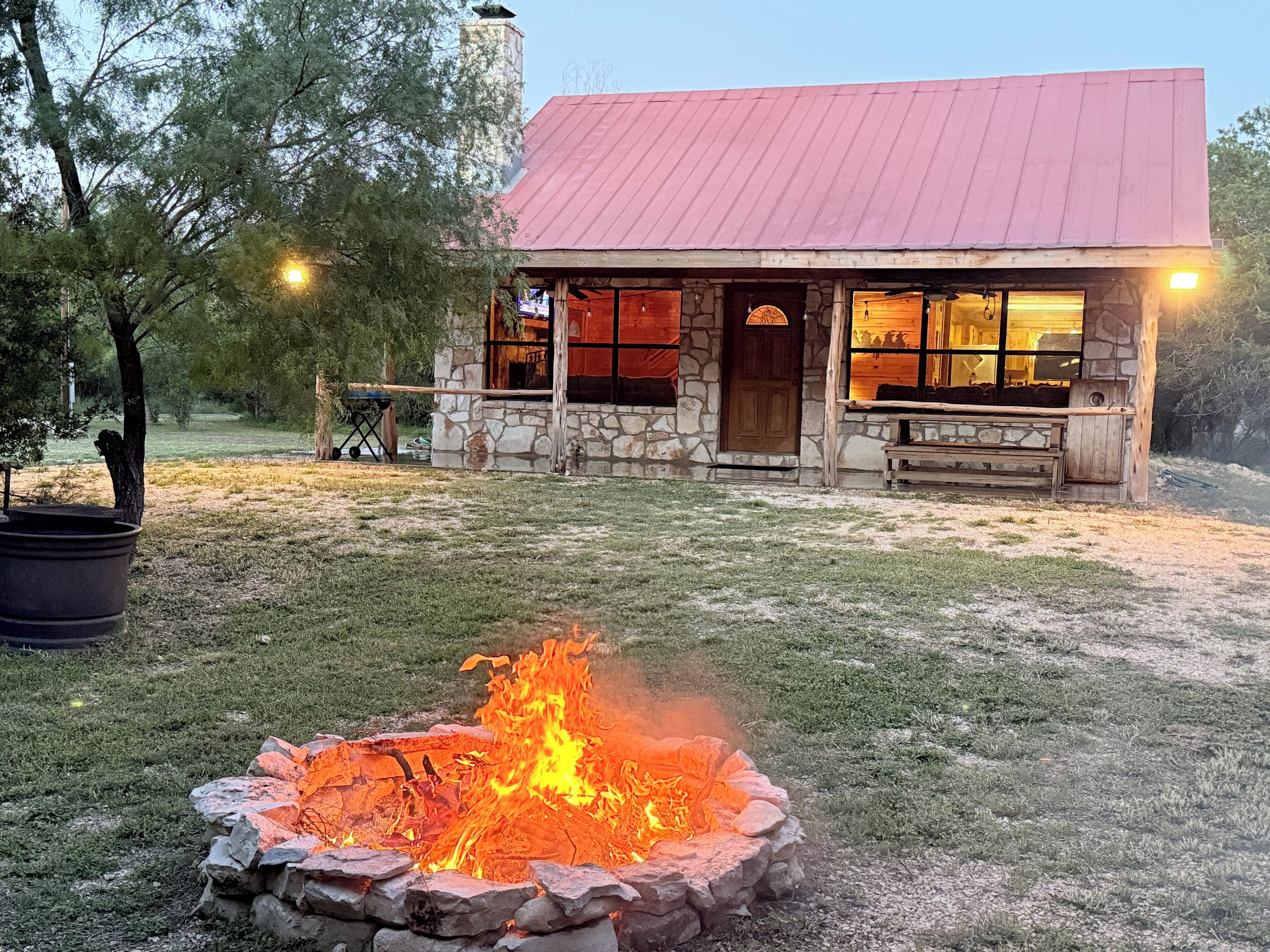 A stone building with a red roof, a fire pit, and a wooden bench.