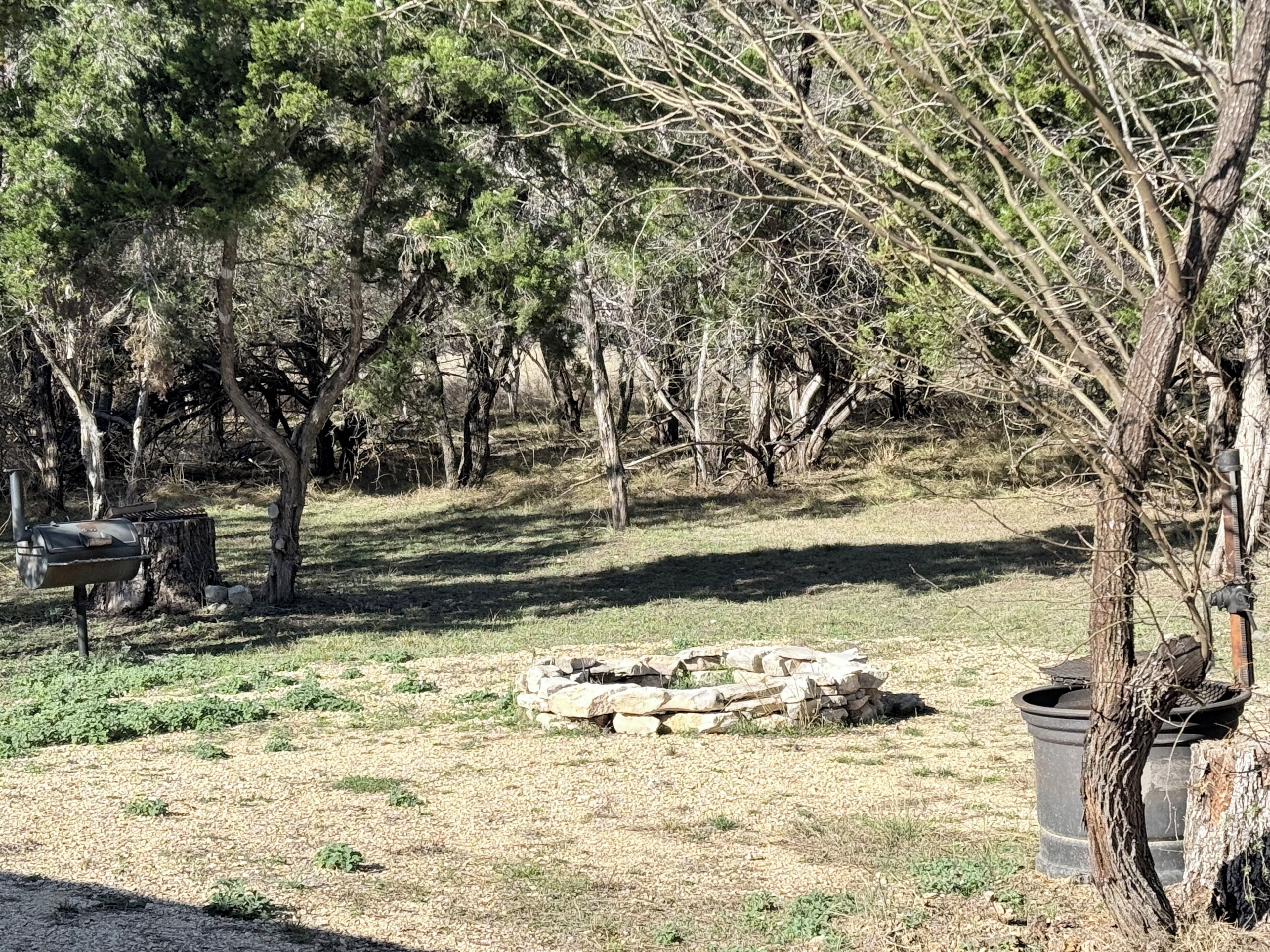 Un cadre extérieur naturel agrémenté d’arbres, d’un barbecue et d’un foyer.