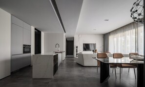 A modern kitchen with a marble island, a dining area with a glass table, and a living space with a TV and curtains. - Wilderness Art Hotel (Chengdu)