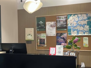 A reception desk with a computer, a bulletin board with various notices, and a flower vase. - Wilderness Art Hotel (Chengdu)