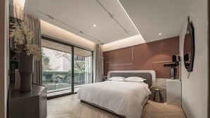 Ein modernes Schlafzimmer mit einem großen Bett, einem Nachttisch, einem Spiegel und Blick auf einen Balkon.