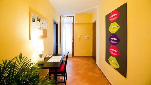 Ein schmaler Flur mit Esstisch und Stühlen, einem Blumentopf und einer Wand mit einem farbenfrohen Kunstwerk.