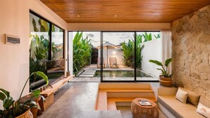 A modern interior with a stone wall, a wooden ceiling, and a large glass door leading to a pool area. - Charming 1-bedroom villa with swimming pool (Tibubeneng)